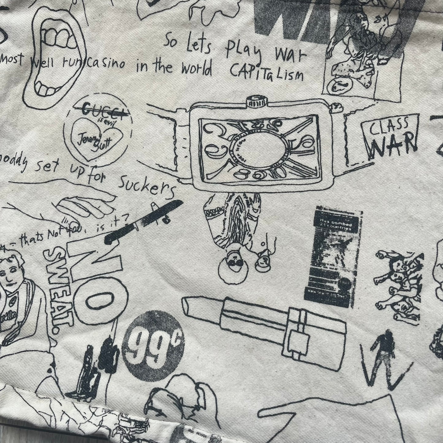 Jeremy Scott 2004 Chicks on Speed: It’s a Project Tote Bag is a cream canvas tote featuring multiple black hand-drawn style graphics including symbols, objects, and abstract motifs such as text elements, crossed-out luxury references, lips, watches, chains, and figures. The bag was originally part of a limited art publication kit released in 2004. It came with additional included items such as a book, poster, CD, clothing pattern, and fabric components as part of the full “Chicks on Speed: It’s a Project” s