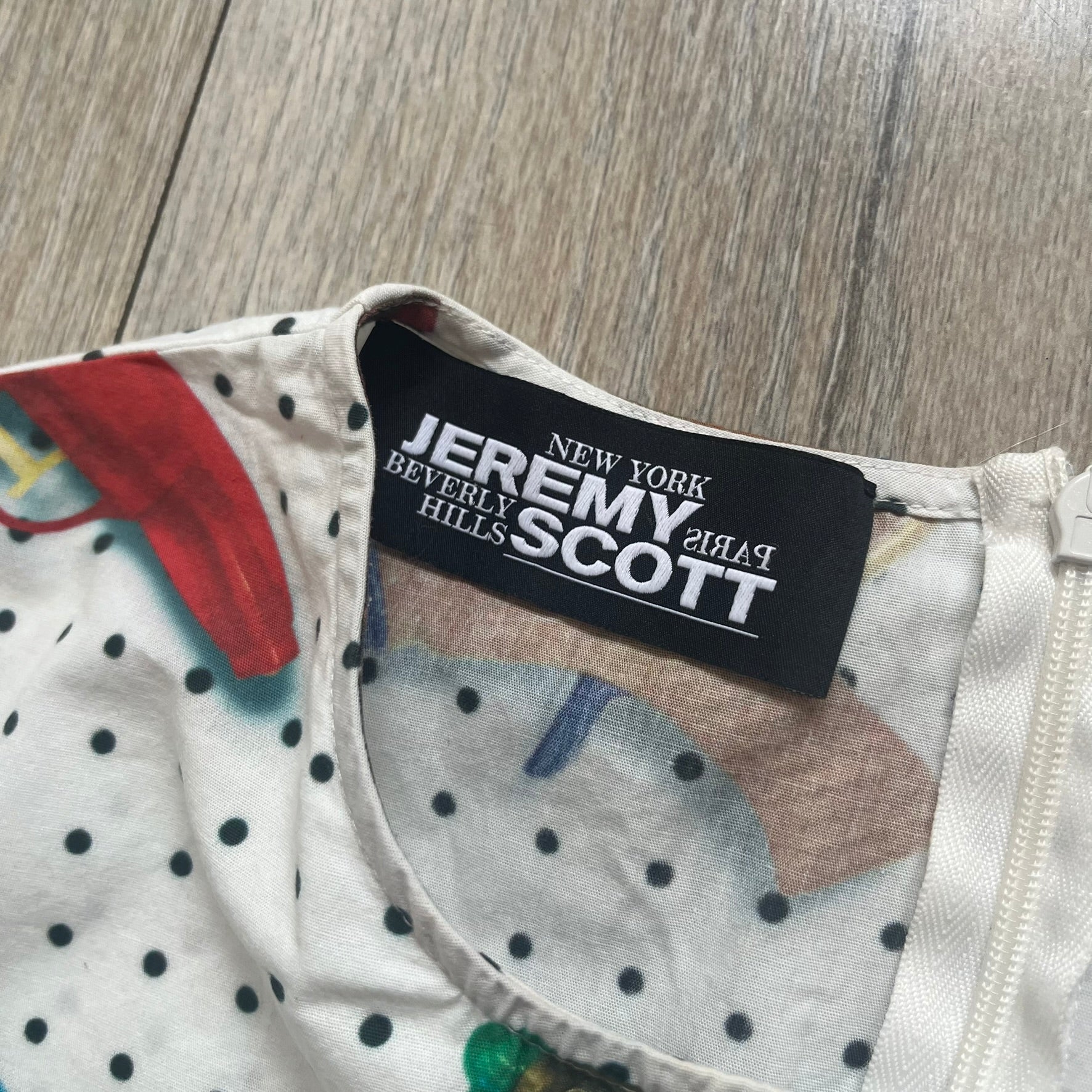 Jeremy Scott SS2016 Watergun Dress is a white flared short dress featuring an all-over print of multicolored realistic waterguns in varying sizes and orientations. The design is set against a black dotted pattern layered across the fabric. It has a fitted upper section with a flared skirt silhouette and includes a black Jeremy Scott neck tag.