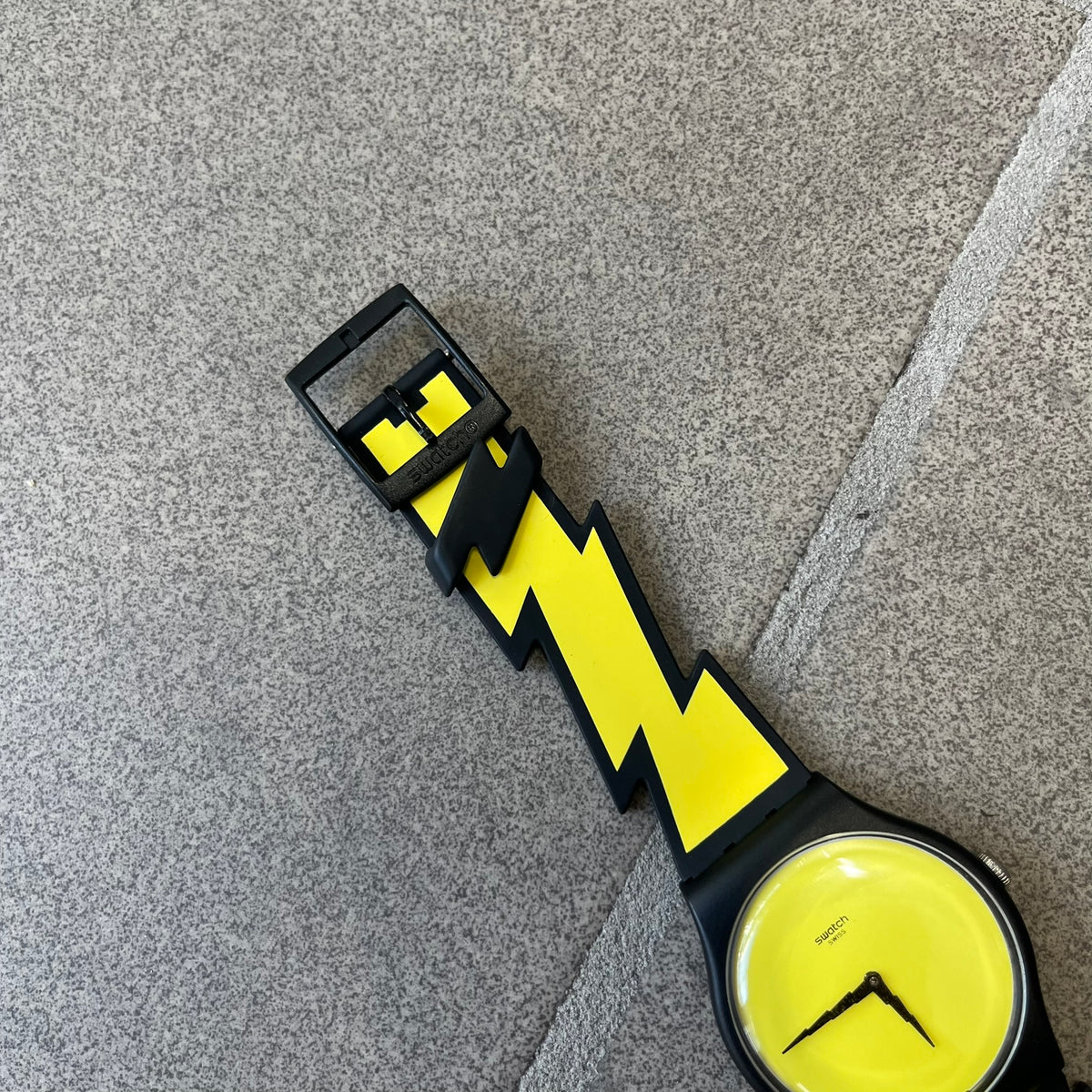 Jeremy Scott Swatch 2011 Lightning Flash Analog Watch (SUOZ104) is a limited-edition watch released in March 2011 from Jeremy Scott's first collaboration with Swatch. It features a black and yellow design with lightning bolt-shaped rubber straps, a yellow dial with a black case, lightning bolt-shaped hands, and a Jeremy Scott signature on the back.