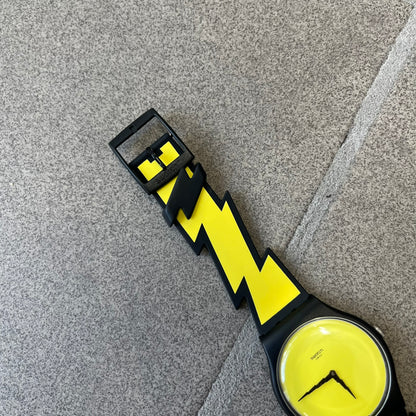 Jeremy Scott Swatch 2011 Lightning Flash Analog Watch (SUOZ104) is a limited-edition watch released in March 2011 from Jeremy Scott's first collaboration with Swatch. It features a black and yellow design with lightning bolt-shaped rubber straps, a yellow dial with a black case, lightning bolt-shaped hands, and a Jeremy Scott signature on the back.