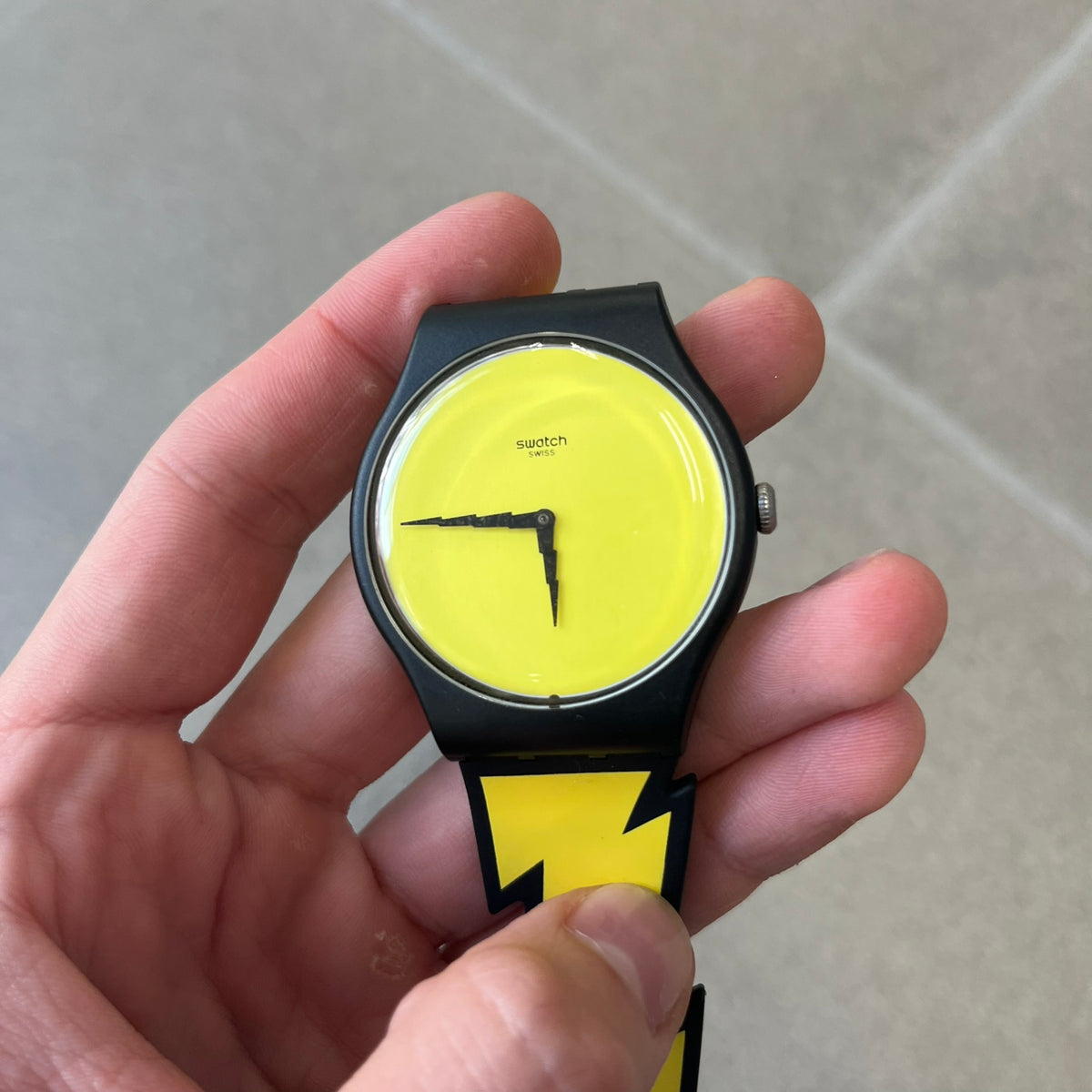 Jeremy Scott Swatch 2011 Lightning Flash Analog Watch (SUOZ104) is a limited-edition watch released in March 2011 from Jeremy Scott's first collaboration with Swatch. It features a black and yellow design with lightning bolt-shaped rubber straps, a yellow dial with a black case, lightning bolt-shaped hands, and a Jeremy Scott signature on the back.