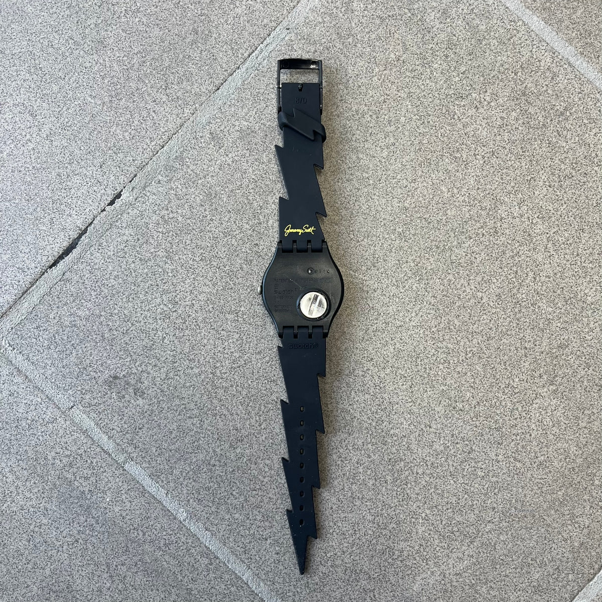 Jeremy Scott Swatch 2011 Lightning Flash Analog Watch (SUOZ104) is a limited-edition watch released in March 2011 from Jeremy Scott's first collaboration with Swatch. It features a black and yellow design with lightning bolt-shaped rubber straps, a yellow dial with a black case, lightning bolt-shaped hands, and a Jeremy Scott signature on the back.