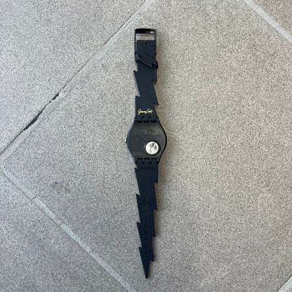 Jeremy Scott Swatch 2011 Lightning Flash Analog Watch (SUOZ104) is a limited-edition watch released in March 2011 from Jeremy Scott's first collaboration with Swatch. It features a black and yellow design with lightning bolt-shaped rubber straps, a yellow dial with a black case, lightning bolt-shaped hands, and a Jeremy Scott signature on the back.