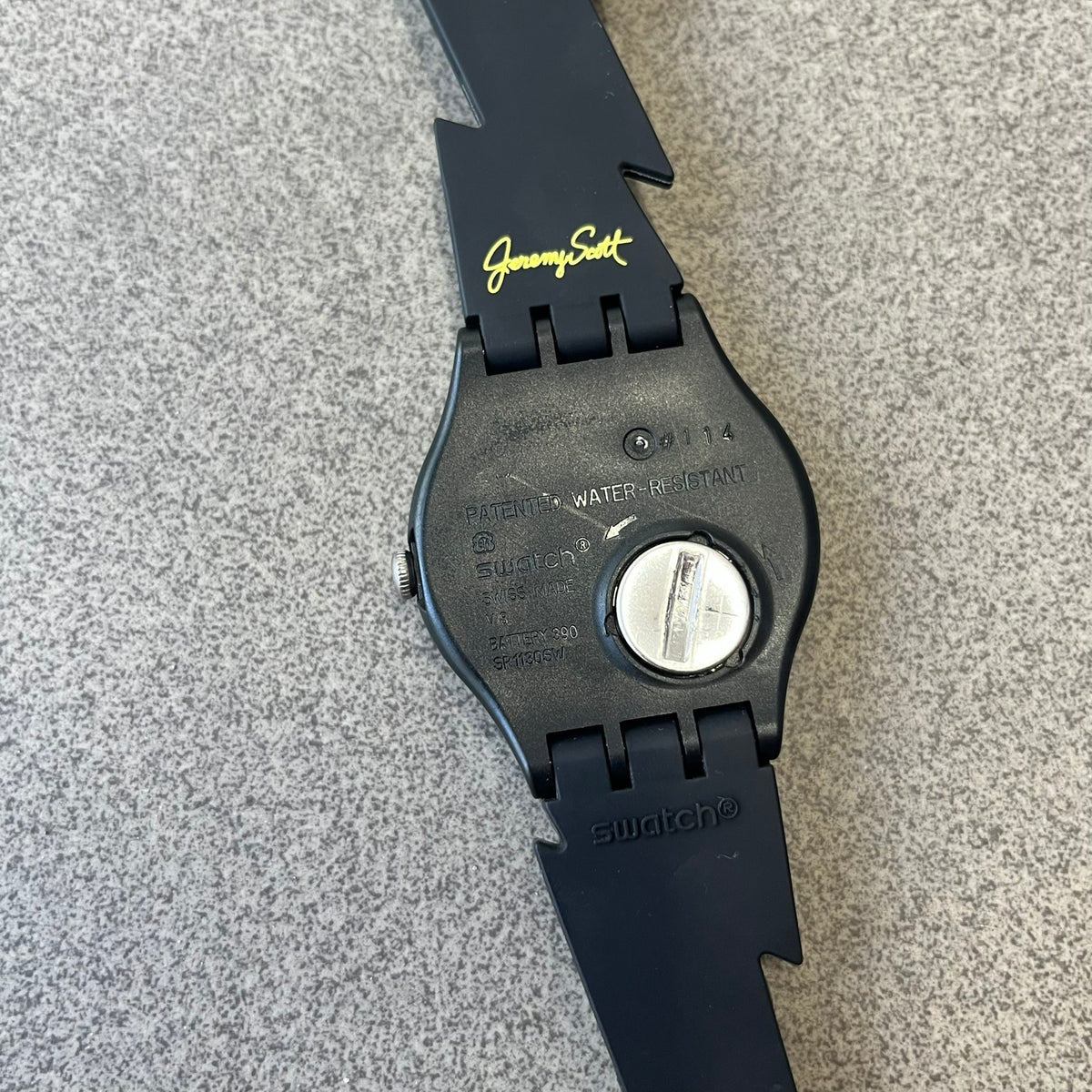 Jeremy Scott Swatch 2011 Lightning Flash Analog Watch (SUOZ104) is a limited-edition watch released in March 2011 from Jeremy Scott's first collaboration with Swatch. It features a black and yellow design with lightning bolt-shaped rubber straps, a yellow dial with a black case, lightning bolt-shaped hands, and a Jeremy Scott signature on the back.