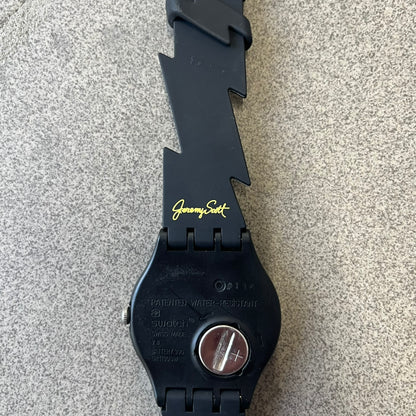Jeremy Scott Swatch 2011 Lightning Flash Analog Watch (SUOZ104) is a limited-edition watch released in March 2011 from Jeremy Scott's first collaboration with Swatch. It features a black and yellow design with lightning bolt-shaped rubber straps, a yellow dial with a black case, lightning bolt-shaped hands, and a Jeremy Scott signature on the back.