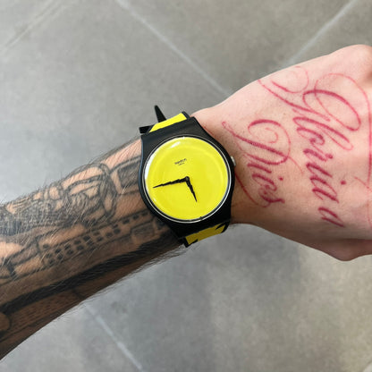 Jeremy Scott Swatch 2011 Lightning Flash Analog Watch (SUOZ104) is a limited-edition watch released in March 2011 from Jeremy Scott's first collaboration with Swatch. It features a black and yellow design with lightning bolt-shaped rubber straps, a yellow dial with a black case, lightning bolt-shaped hands, and a Jeremy Scott signature on the back.