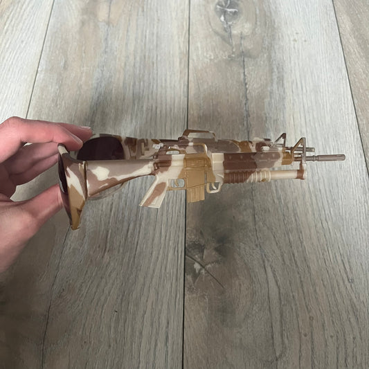 Jeremy Scott x Linda Farrow SS2013 Desert Camo M16 Rifle Sunglasses (JSARMYC4SUN) are a statement eyewear piece from the Spring/Summer 2013 collaboration. The design features full camo brown and beige frames with red/pink lenses, while the arms are constructed as detailed 3D M16 rifle shapes extending toward the front of the frame. The model includes Jeremy Scott branding on the inner arms and is produced in a high-detail acetate construction.