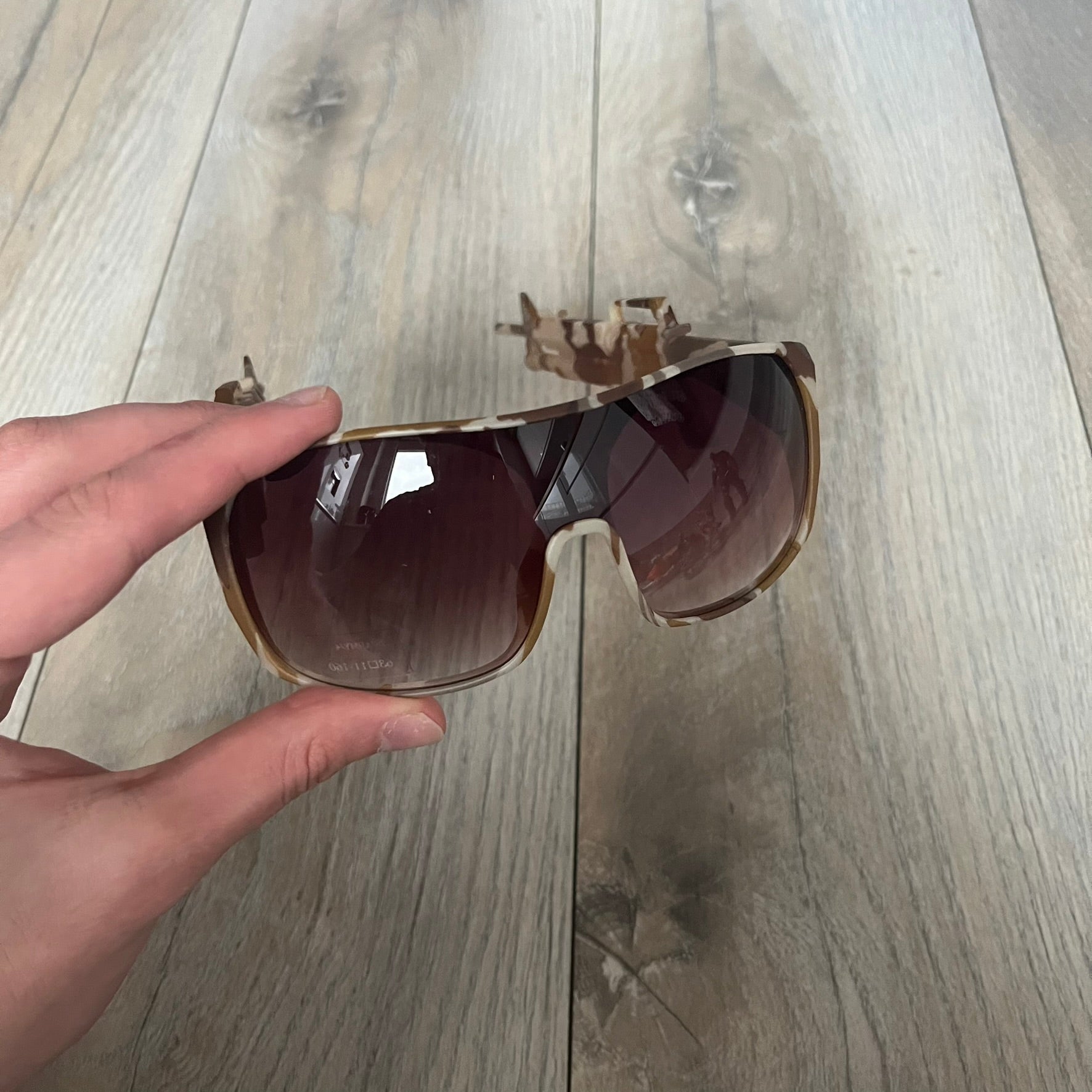 Jeremy Scott x Linda Farrow SS2013 Desert Camo M16 Rifle Sunglasses (JSARMYC4SUN) are a statement eyewear piece from the Spring/Summer 2013 collaboration. The design features full camo brown and beige frames with red/pink lenses, while the arms are constructed as detailed 3D M16 rifle shapes extending toward the front of the frame. The model includes Jeremy Scott branding on the inner arms and is produced in a high-detail acetate construction.