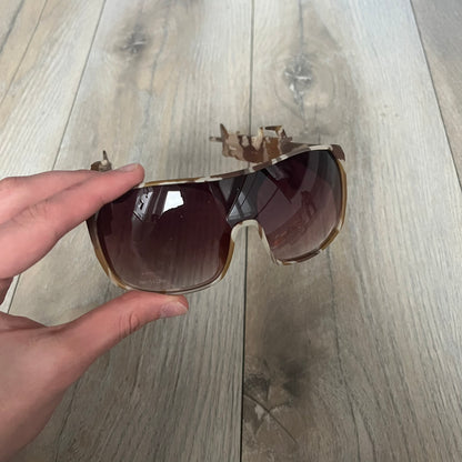 Jeremy Scott x Linda Farrow SS2013 Desert Camo M16 Rifle Sunglasses (JSARMYC4SUN) are a statement eyewear piece from the Spring/Summer 2013 collaboration. The design features full camo brown and beige frames with red/pink lenses, while the arms are constructed as detailed 3D M16 rifle shapes extending toward the front of the frame. The model includes Jeremy Scott branding on the inner arms and is produced in a high-detail acetate construction.