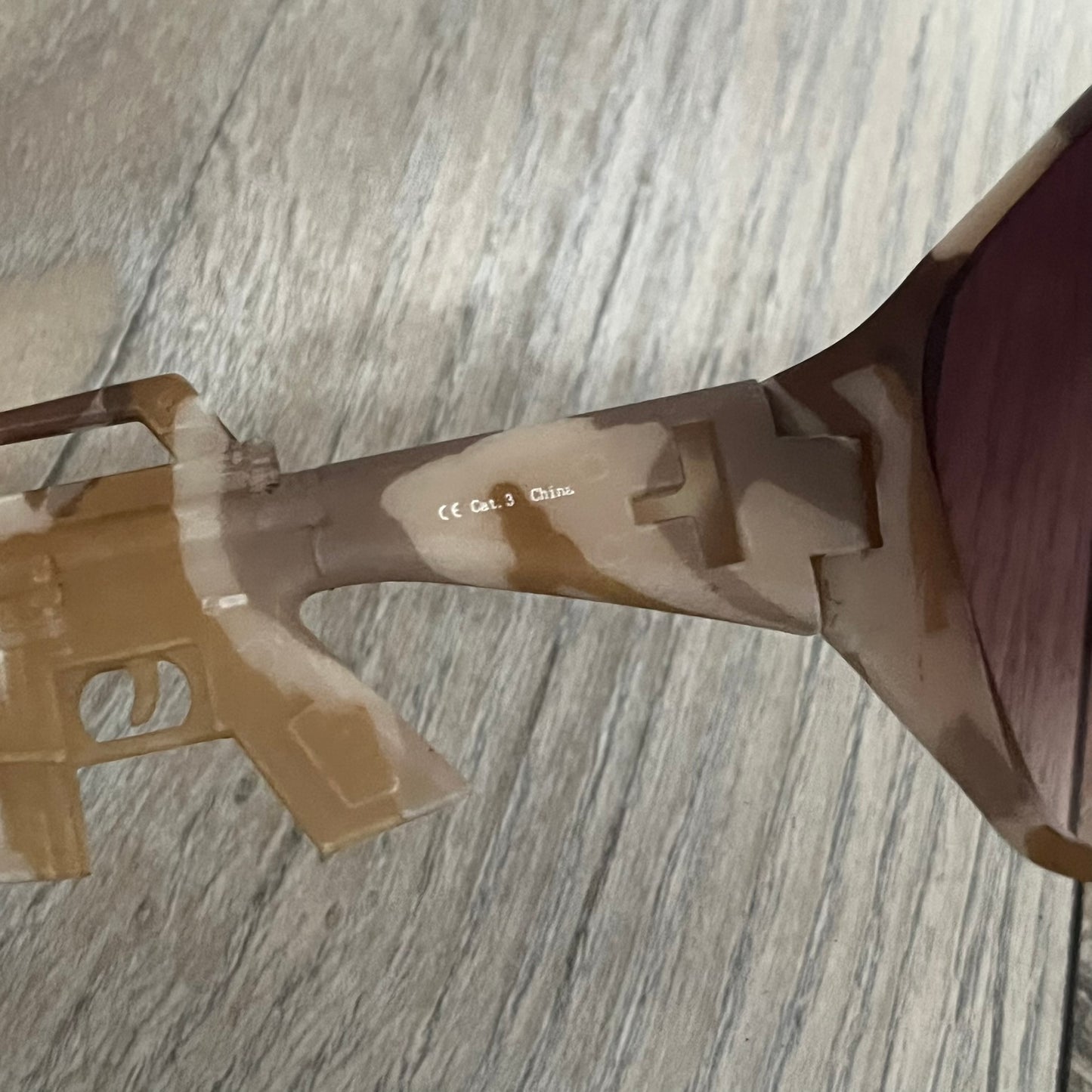 Jeremy Scott x Linda Farrow SS2013 Desert Camo M16 Rifle Sunglasses (JSARMYC4SUN) are a statement eyewear piece from the Spring/Summer 2013 collaboration. The design features full camo brown and beige frames with red/pink lenses, while the arms are constructed as detailed 3D M16 rifle shapes extending toward the front of the frame. The model includes Jeremy Scott branding on the inner arms and is produced in a high-detail acetate construction.