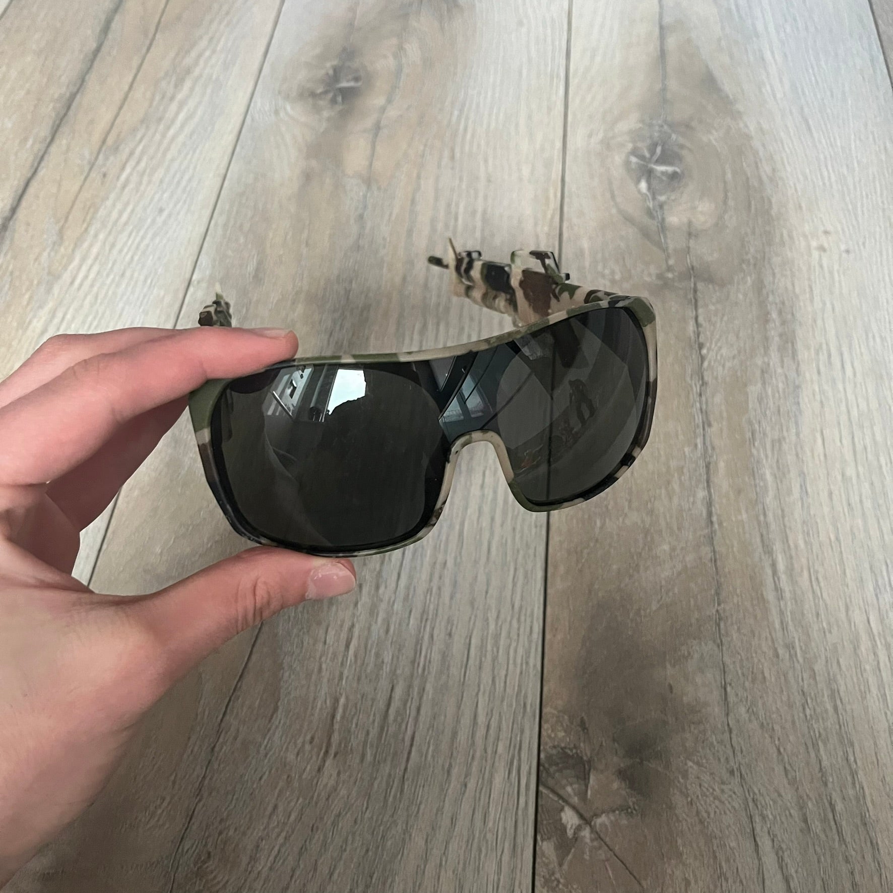 Jeremy Scott x Linda Farrow SS2013 Green Camo M16 Rifle Sunglasses (JSARMYC3SUN) are a statement eyewear piece from the Spring/Summer 2013 collaboration. The design features full camo green, brown, and beige frames with dark lenses, while the arms are constructed as detailed 3D M16 rifle shapes extending toward the front of the frame. The model includes Jeremy Scott branding on the inner arms and is produced in a high-detail acetate construction.