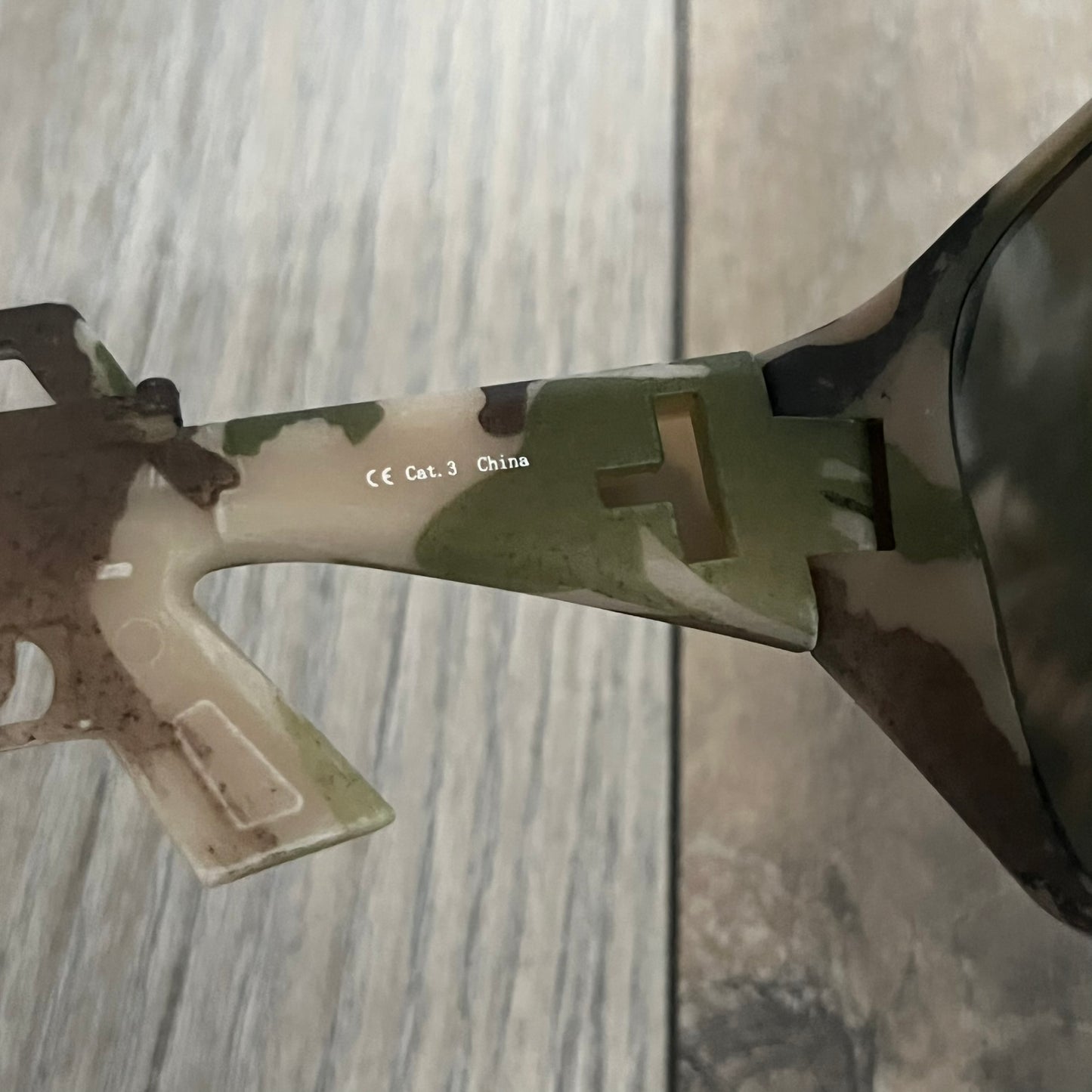 Jeremy Scott x Linda Farrow SS2013 Green Camo M16 Rifle Sunglasses (JSARMYC3SUN) are a statement eyewear piece from the Spring/Summer 2013 collaboration. The design features full camo green, brown, and beige frames with dark lenses, while the arms are constructed as detailed 3D M16 rifle shapes extending toward the front of the frame. The model includes Jeremy Scott branding on the inner arms and is produced in a high-detail acetate construction.