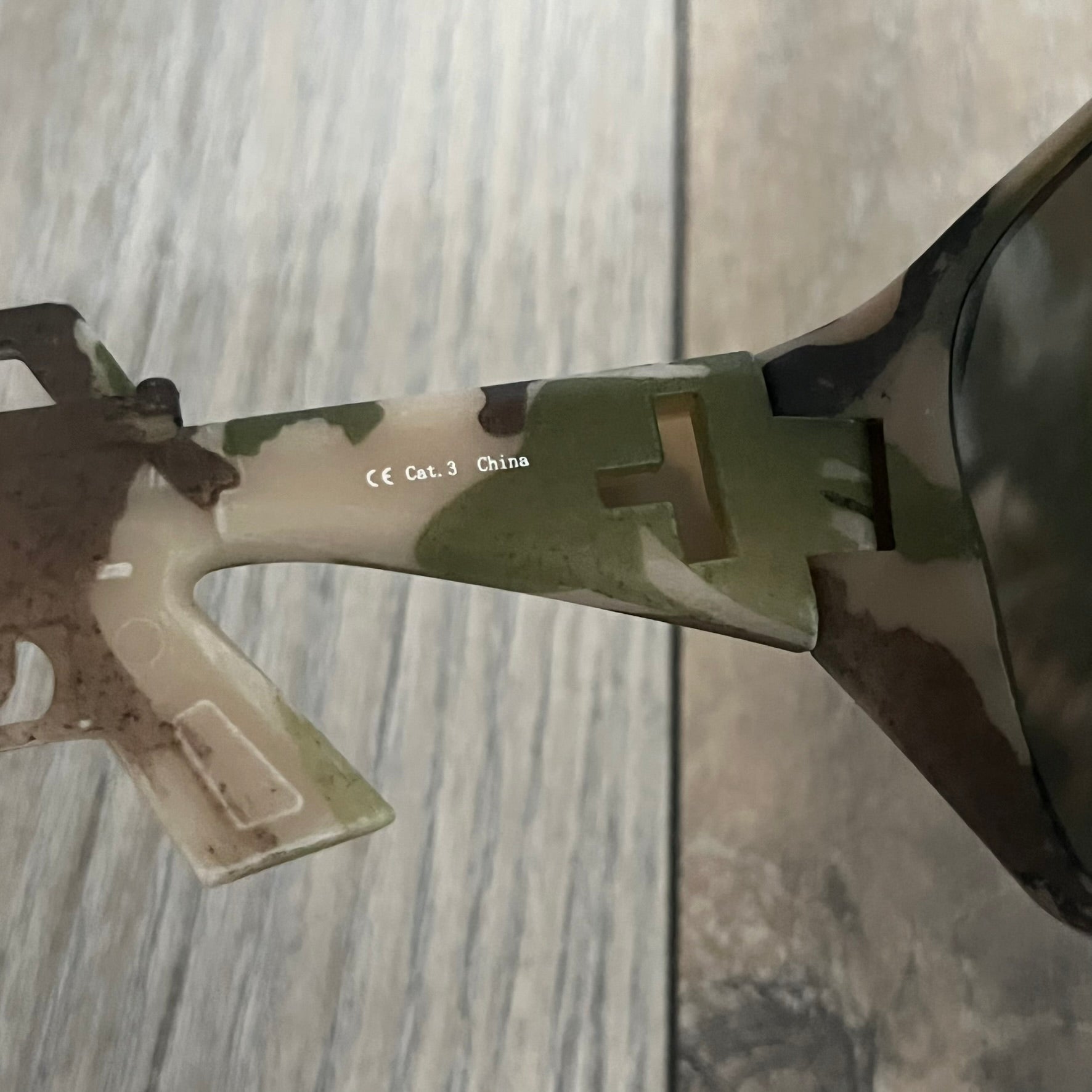 Jeremy Scott x Linda Farrow SS2013 Green Camo M16 Rifle Sunglasses (JSARMYC3SUN) are a statement eyewear piece from the Spring/Summer 2013 collaboration. The design features full camo green, brown, and beige frames with dark lenses, while the arms are constructed as detailed 3D M16 rifle shapes extending toward the front of the frame. The model includes Jeremy Scott branding on the inner arms and is produced in a high-detail acetate construction.