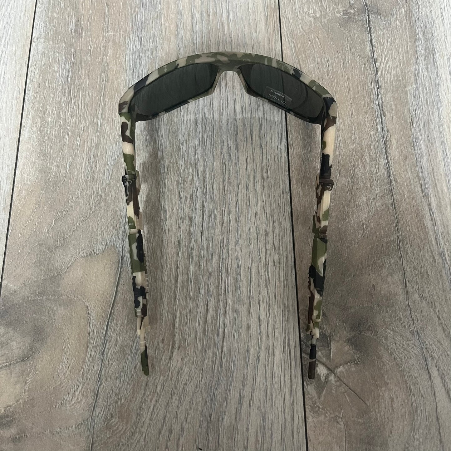Jeremy Scott x Linda Farrow SS2013 Green Camo M16 Rifle Sunglasses (JSARMYC3SUN) are a statement eyewear piece from the Spring/Summer 2013 collaboration. The design features full camo green, brown, and beige frames with dark lenses, while the arms are constructed as detailed 3D M16 rifle shapes extending toward the front of the frame. The model includes Jeremy Scott branding on the inner arms and is produced in a high-detail acetate construction.
