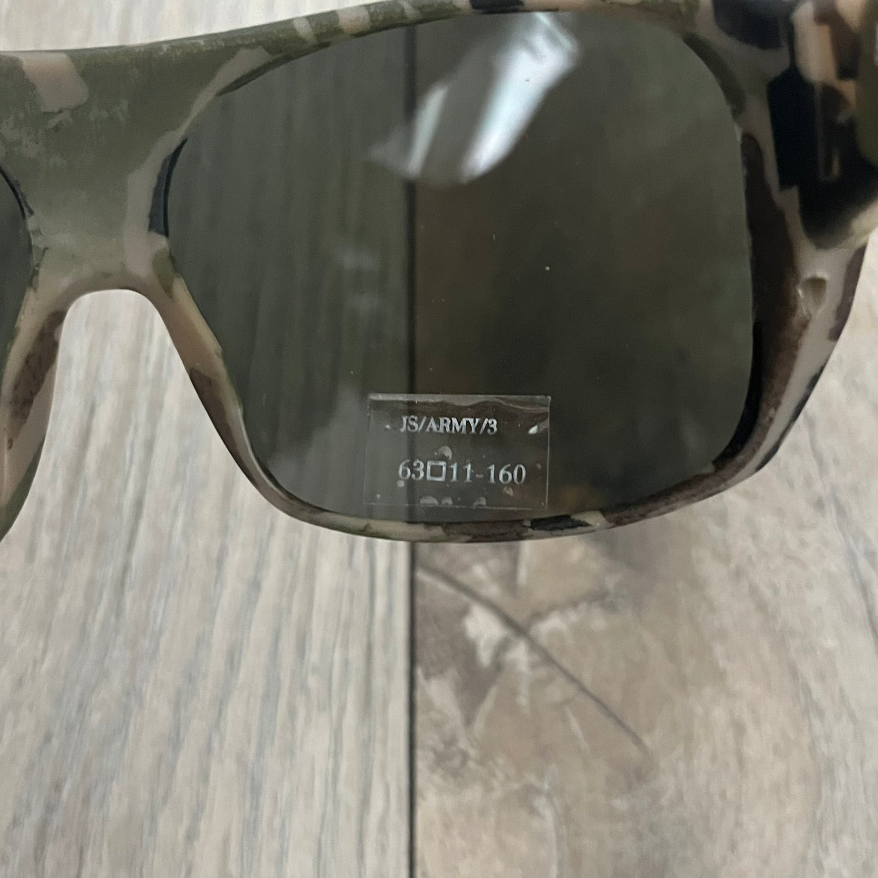 Jeremy Scott x Linda Farrow SS2013 Green Camo M16 Rifle Sunglasses (JSARMYC3SUN) are a statement eyewear piece from the Spring/Summer 2013 collaboration. The design features full camo green, brown, and beige frames with dark lenses, while the arms are constructed as detailed 3D M16 rifle shapes extending toward the front of the frame. The model includes Jeremy Scott branding on the inner arms and is produced in a high-detail acetate construction.