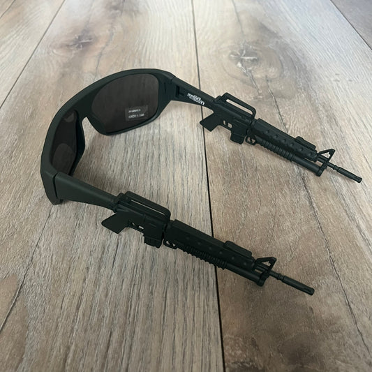 Jeremy Scott x Linda Farrow SS2013 Matt Khaki M16 Rifle Sunglasses (JSARMYC5SUN) are a statement eyewear piece from the Spring/Summer 2013 collaboration. The design features full matt dark khaki frames with black lenses, while the arms are constructed as detailed 3D M16 rifle shapes extending toward the front of the frame. The model includes Jeremy Scott branding on the inner arms and is produced in a high-detail acetate construction.