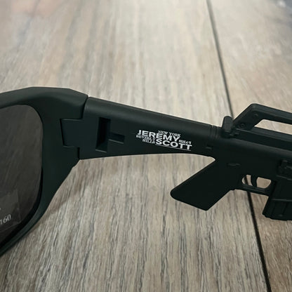 Jeremy Scott x Linda Farrow SS2013 Matt Khaki M16 Rifle Sunglasses (JSARMYC5SUN) are a statement eyewear piece from the Spring/Summer 2013 collaboration. The design features full matt dark khaki frames with black lenses, while the arms are constructed as detailed 3D M16 rifle shapes extending toward the front of the frame. The model includes Jeremy Scott branding on the inner arms and is produced in a high-detail acetate construction.