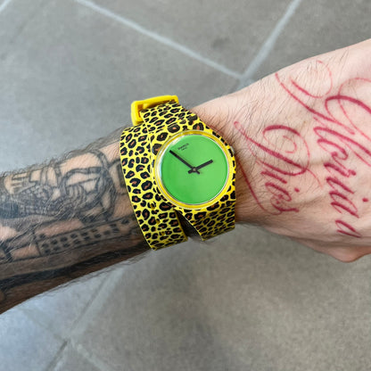 Swatch x Jeremy Scott 2011 Punk Analog Watch GZ251 is a quartz watch from the Gent Original line featuring a bright green dial with black hands and a plastic case. The design includes a comically long silicone strap with leopard print that wraps twice around the wrist, secured with multiple yellow loops, and Jeremy Scott branding on the upper strap.
