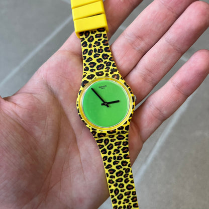 Swatch x Jeremy Scott 2011 Punk Analog Watch GZ251 is a quartz watch from the Gent Original line featuring a bright green dial with black hands and a plastic case. The design includes a comically long silicone strap with leopard print that wraps twice around the wrist, secured with multiple yellow loops, and Jeremy Scott branding on the upper strap.