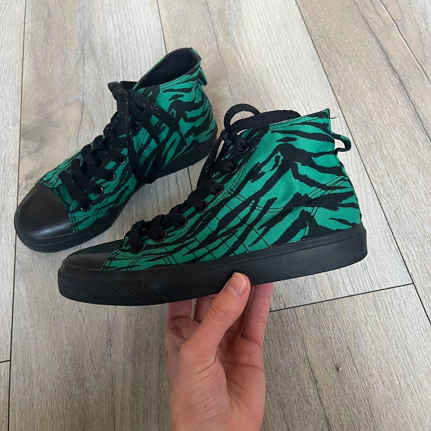Jeremy Scott x adidas 2014 Nizza Hi “Forest Green” Sneakers are made with a forest green canvas upper featuring an all-over black tiger print. The high-top shoes include rubber soles and standard adidas Nizza tooling. This model was released in 2014 in a green and black colorway as part of the Jeremy Scott x adidas collaboration.