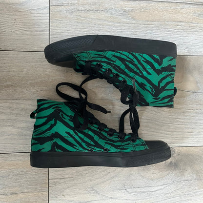 Jeremy Scott x adidas 2014 Nizza Hi “Forest Green” Sneakers are made with a forest green canvas upper featuring an all-over black tiger print. The high-top shoes include rubber soles and standard adidas Nizza tooling. This model was released in 2014 in a green and black colorway as part of the Jeremy Scott x adidas collaboration.