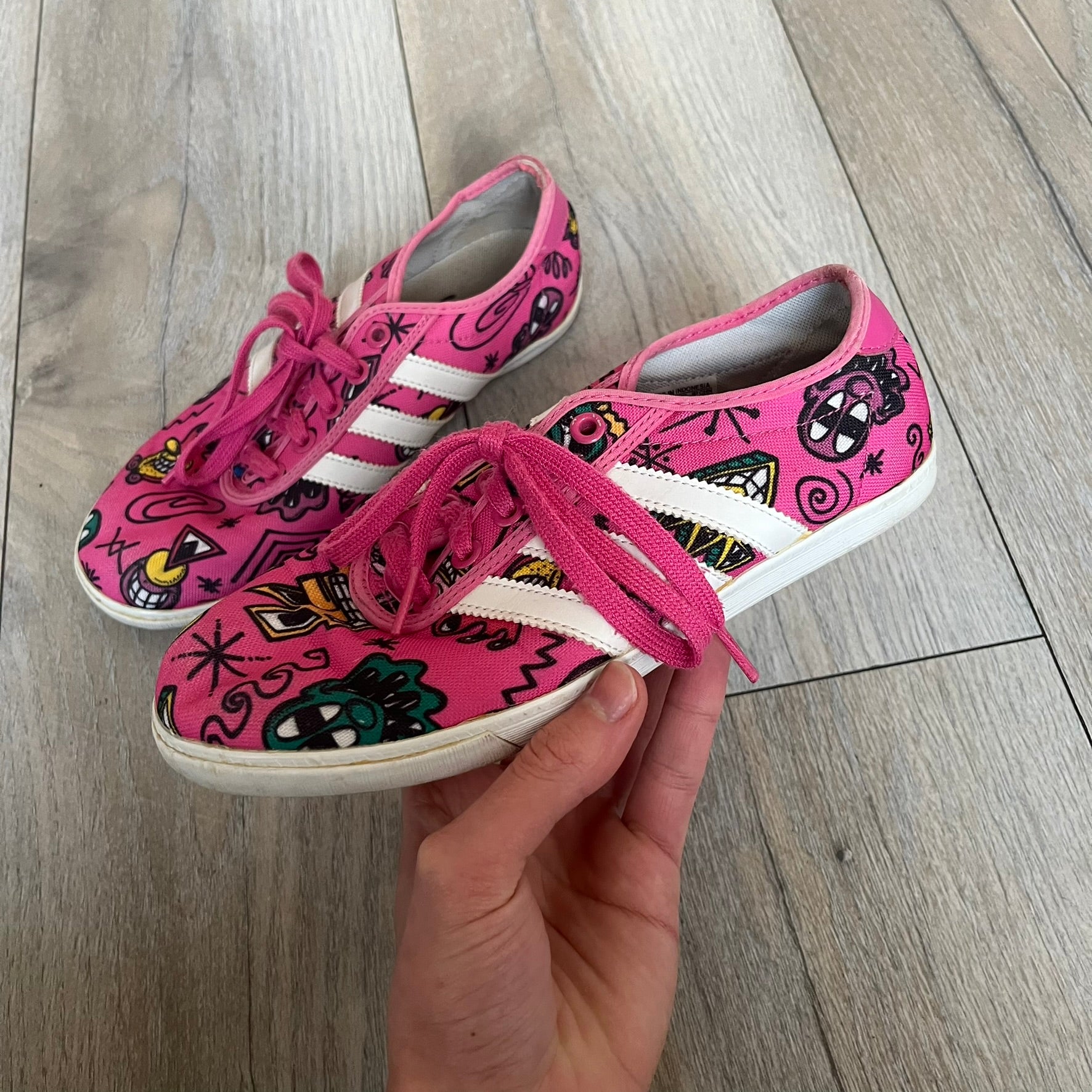 Jeremy Scott x adidas 2014 P-Sole “Pink” Sneakers feature a pink canvas upper with white leather adidas stripes and multicolored graphic prints. Released in 2014, they are part of the P-Sole line in the collaboration between adidas Originals, Jeremy Scott, and Kenny Scharf. The shoes include standard rubber soles and lace-up closure.