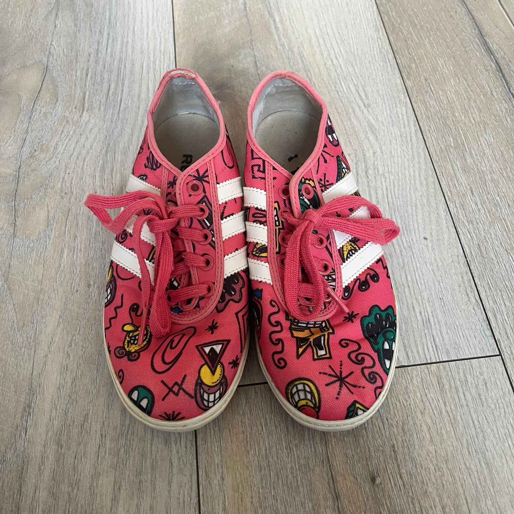 Jeremy Scott x adidas 2014 P-Sole “Pink” Sneakers feature a pink canvas upper with white leather adidas stripes and multicolored graphic prints. Released in 2014, they are part of the P-Sole line in the collaboration between adidas Originals, Jeremy Scott, and Kenny Scharf. The shoes include standard rubber soles and lace-up closure.