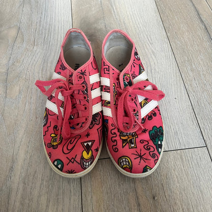 Jeremy Scott x adidas 2014 P-Sole “Pink” Sneakers feature a pink canvas upper with white leather adidas stripes and multicolored graphic prints. Released in 2014, they are part of the P-Sole line in the collaboration between adidas Originals, Jeremy Scott, and Kenny Scharf. The shoes include standard rubber soles and lace-up closure.
