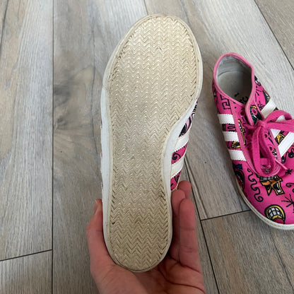 Jeremy Scott x adidas 2014 P-Sole “Pink” Sneakers feature a pink canvas upper with white leather adidas stripes and multicolored graphic prints. Released in 2014, they are part of the P-Sole line in the collaboration between adidas Originals, Jeremy Scott, and Kenny Scharf. The shoes include standard rubber soles and lace-up closure.
