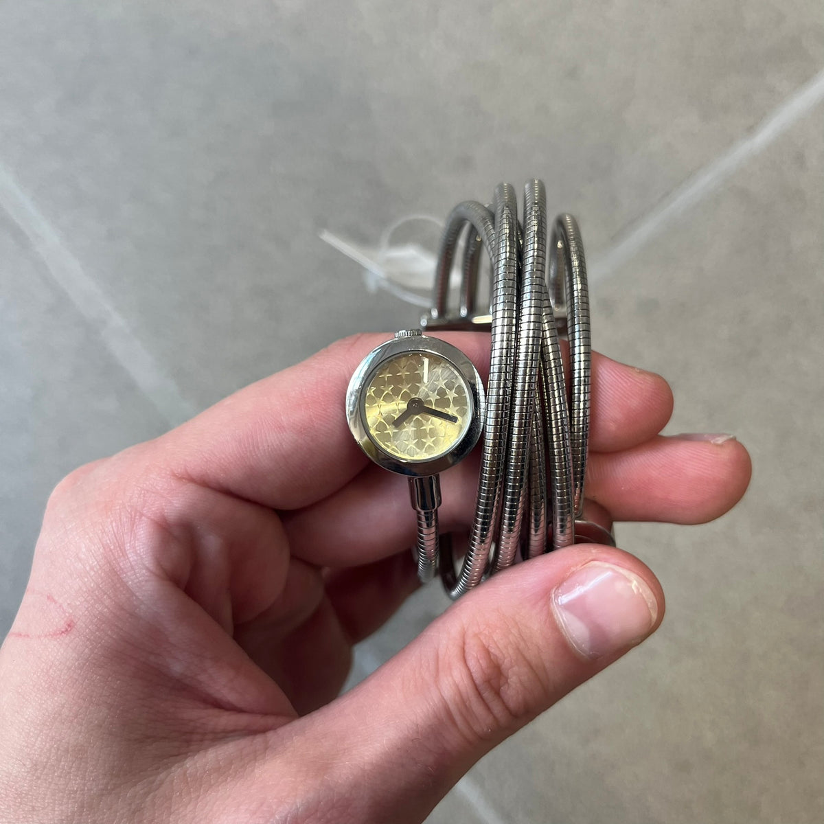 Just Cavalli 2000’s Yellow Stars Bracelet Watch is a stretch metal bracelet watch from Just Cavalli featuring multiple intersecting silver-tone coil bands that create a layered wrap-around design. One end of the bracelet holds a small round analog watch with a yellow dial finished with a textured star pattern, while the opposite end features a circular metal element engraved with the JC logo. The bracelet uses a spring-style stretch construction instead of a clasp, allowing it to expand to fit the wrist. Th