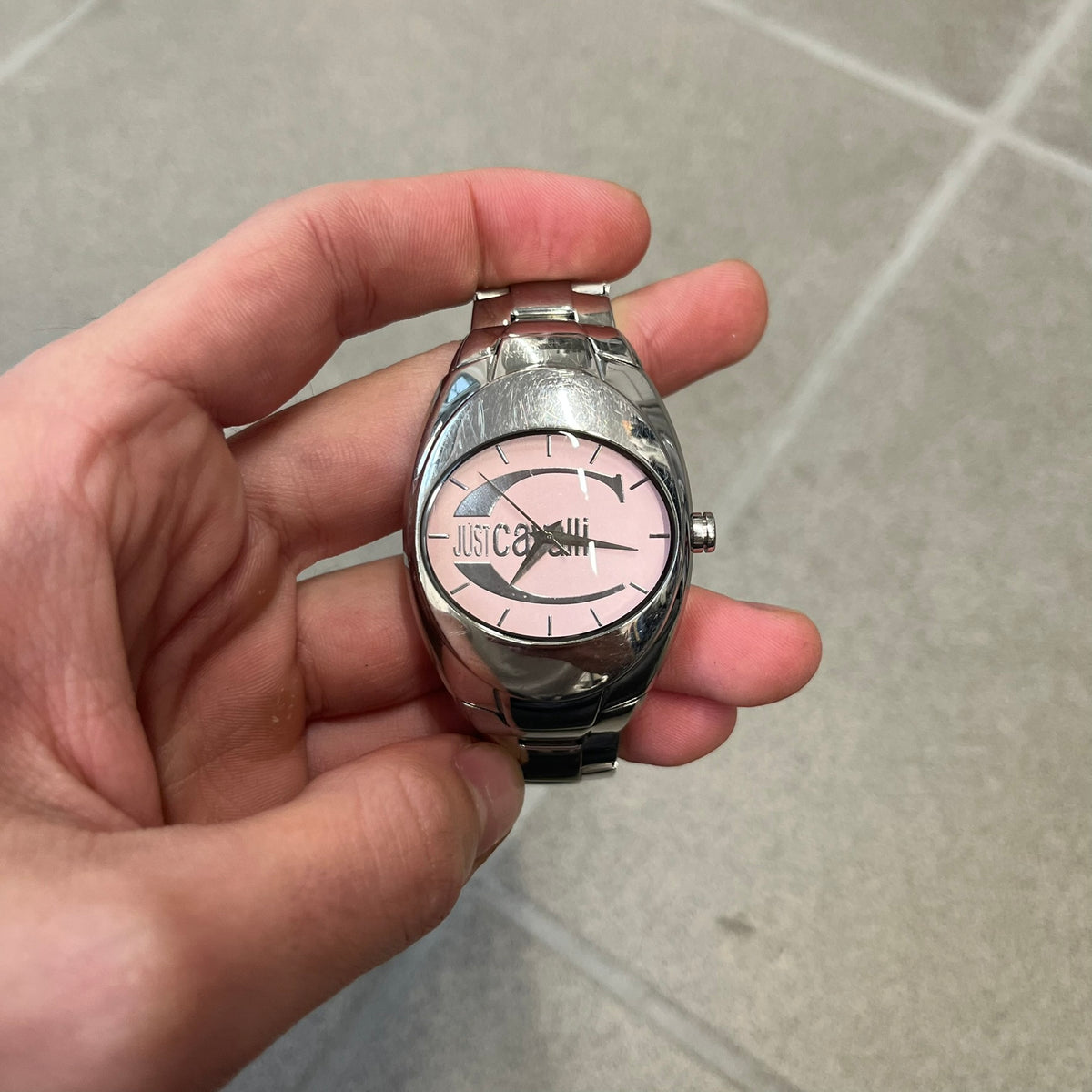 Just Cavalli 2010’s Pink Dial Analog Watch is a stainless steel watch with a raised oval case and an oval pink dial with a large silver Just Cavalli logo. The clasp is Just Cavalli branded, and the watch comes with its box and papers.