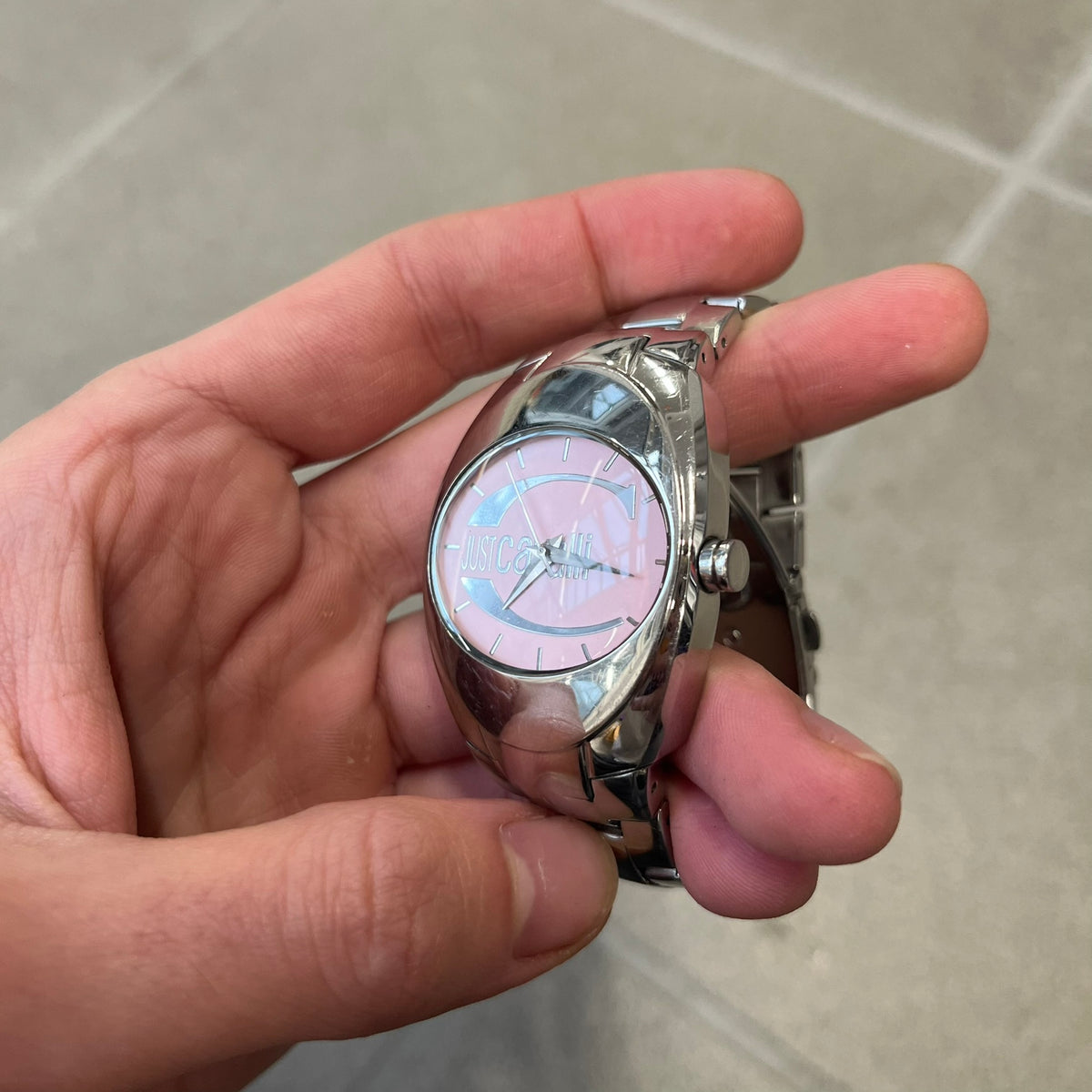 Just Cavalli 2010’s Pink Dial Analog Watch is a stainless steel watch with a raised oval case and an oval pink dial with a large silver Just Cavalli logo. The clasp is Just Cavalli branded, and the watch comes with its box and papers.
