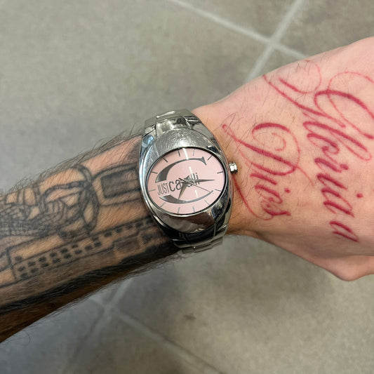Just Cavalli 2010’s Pink Dial Analog Watch is a stainless steel watch with a raised oval case and an oval pink dial with a large silver Just Cavalli logo. The clasp is Just Cavalli branded, and the watch comes with its box and papers.
