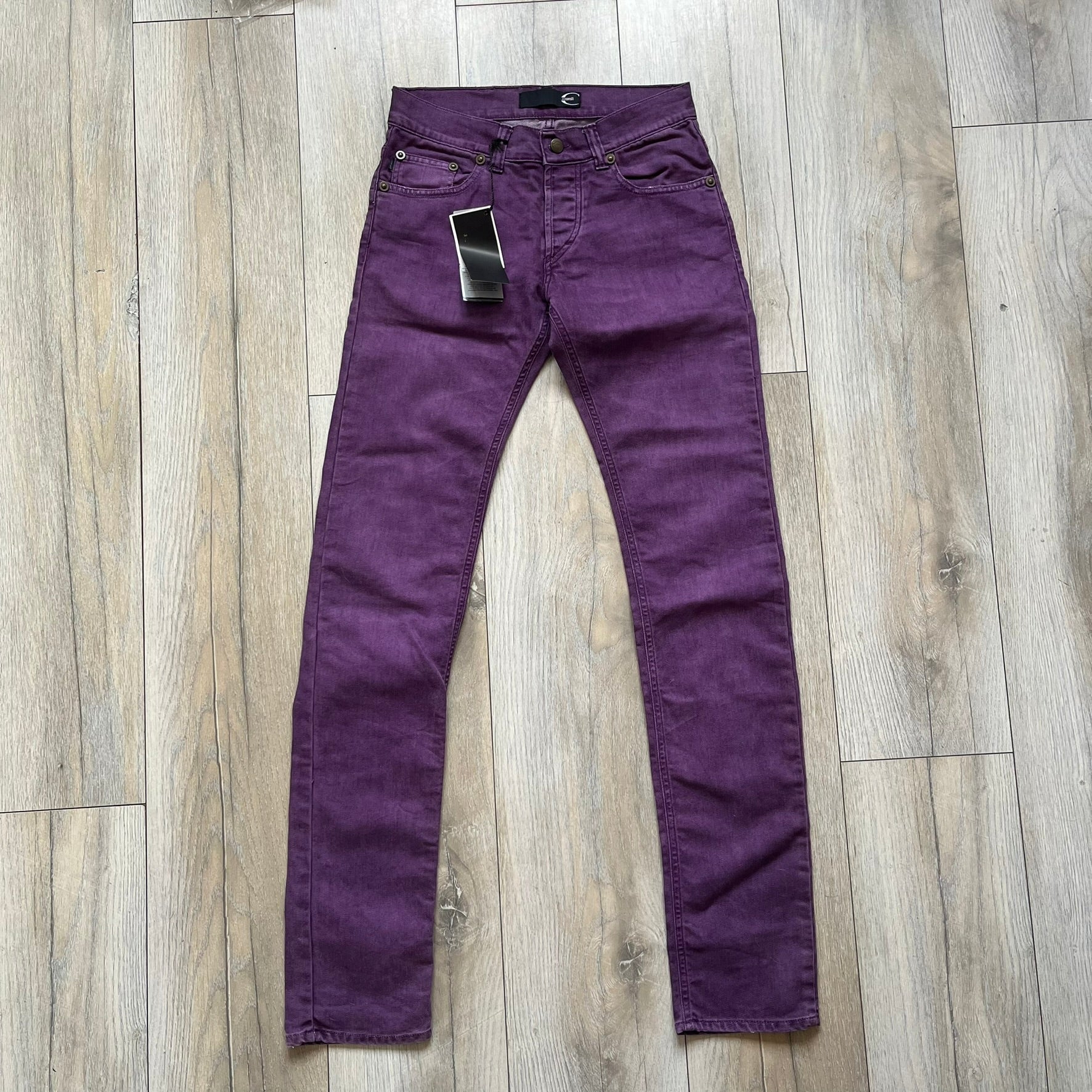 Just Cavalli 2010s Purple Slim Jeans are slim-fit denim jeans finished in a full purple colorway. The pair features classic front and back pocket construction, branded metal button closure, and small metal stud details on the pockets. Additional details include a rear leather Just Cavalli logo patch, interior Just Cavalli tag, and original paper tag.