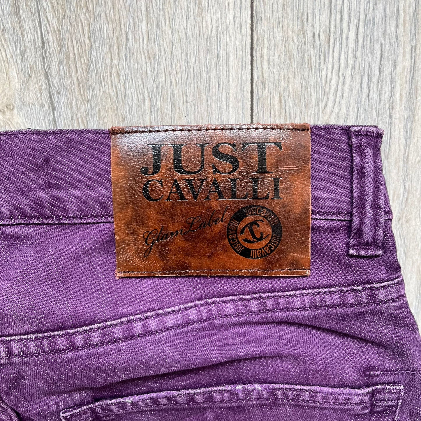 Just Cavalli 2010s Purple Slim Jeans are slim-fit denim jeans finished in a full purple colorway. The pair features classic front and back pocket construction, branded metal button closure, and small metal stud details on the pockets. Additional details include a rear leather Just Cavalli logo patch, interior Just Cavalli tag, and original paper tag.