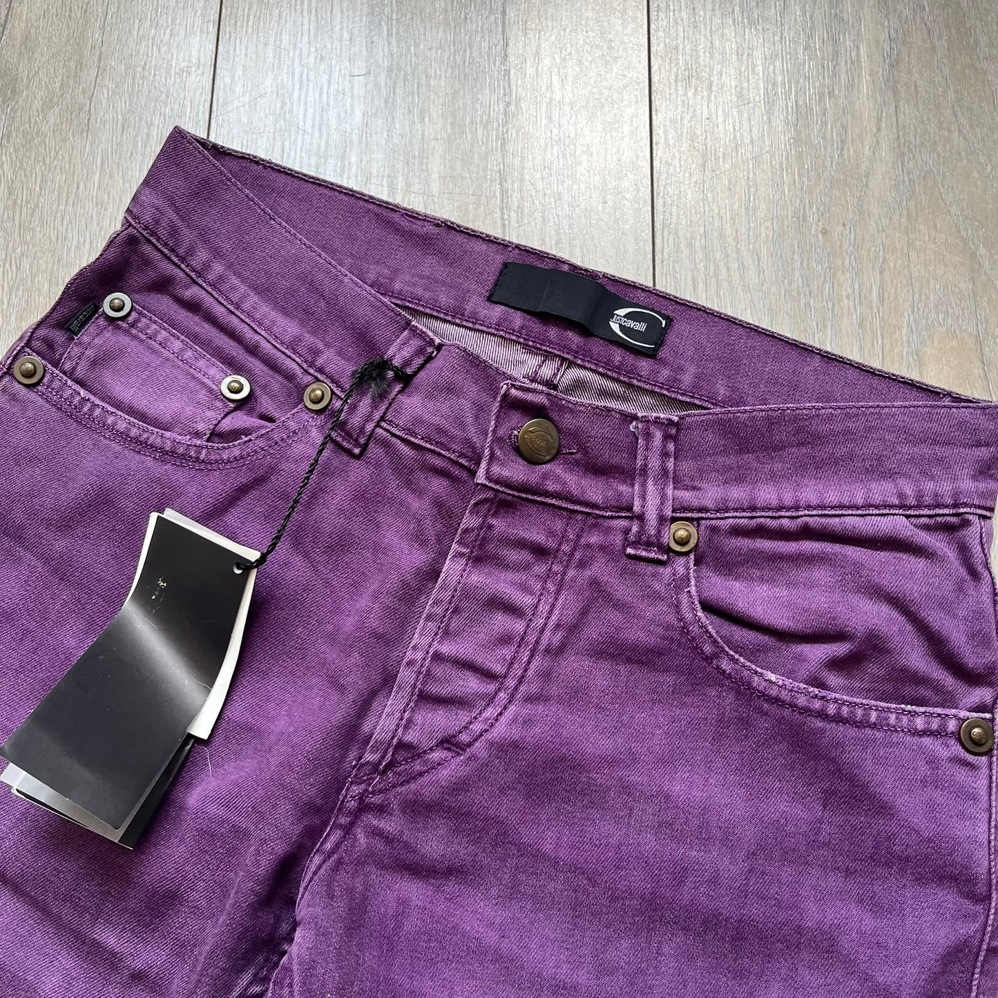 Just Cavalli 2010s Purple Slim Jeans are slim-fit denim jeans finished in a full purple colorway. The pair features classic front and back pocket construction, branded metal button closure, and small metal stud details on the pockets. Additional details include a rear leather Just Cavalli logo patch, interior Just Cavalli tag, and original paper tag.