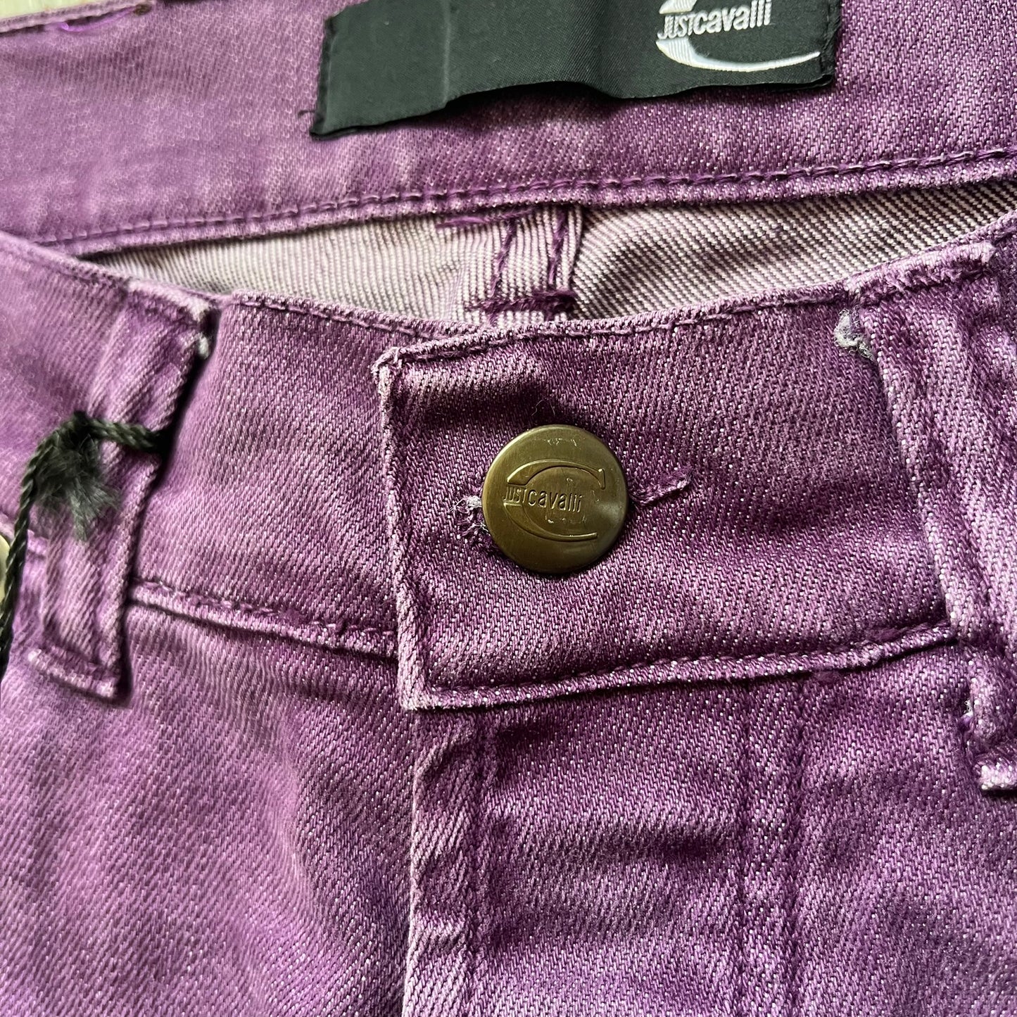 Just Cavalli 2010s Purple Slim Jeans are slim-fit denim jeans finished in a full purple colorway. The pair features classic front and back pocket construction, branded metal button closure, and small metal stud details on the pockets. Additional details include a rear leather Just Cavalli logo patch, interior Just Cavalli tag, and original paper tag.