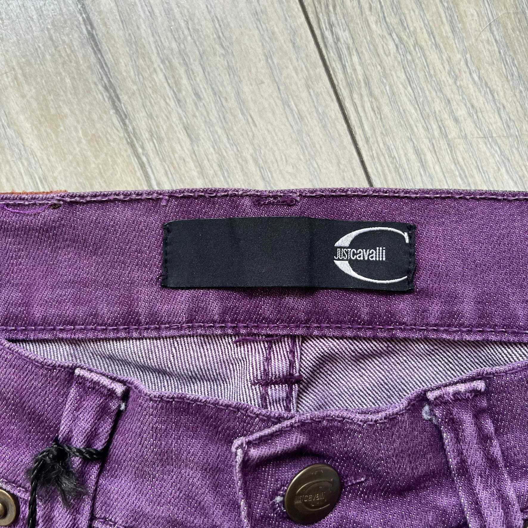 Just Cavalli 2010s Purple Slim Jeans are slim-fit denim jeans finished in a full purple colorway. The pair features classic front and back pocket construction, branded metal button closure, and small metal stud details on the pockets. Additional details include a rear leather Just Cavalli logo patch, interior Just Cavalli tag, and original paper tag.