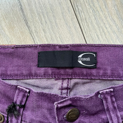 Just Cavalli 2010s Purple Slim Jeans are slim-fit denim jeans finished in a full purple colorway. The pair features classic front and back pocket construction, branded metal button closure, and small metal stud details on the pockets. Additional details include a rear leather Just Cavalli logo patch, interior Just Cavalli tag, and original paper tag.