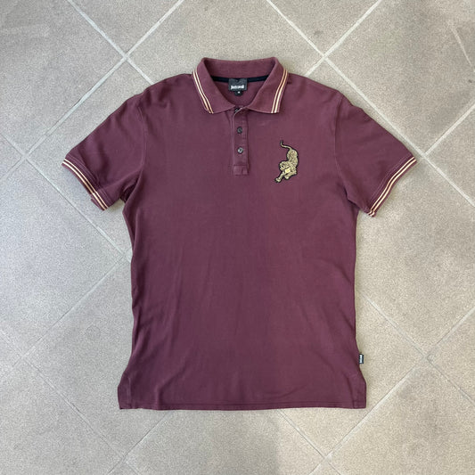 Just Cavalli 2017 Leopard Patch Polo is a burgundy, 100% cotton polo with gold/yellow trim along the hems and collar, featuring a roaring leopard patch on the chest and a small Cavalli side tag. It has side vents at the hem, typical of the polo style.