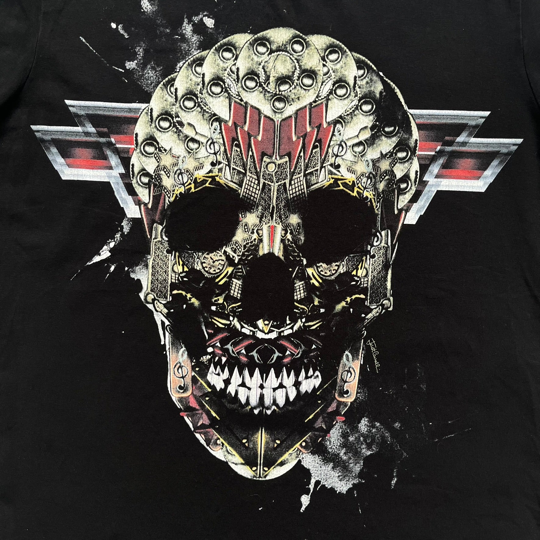 Just Cavalli AW2016 Metal Skull Print Black Tee is a black cotton T-shirt featuring a detailed front graphic of a metallic-style skull composed of gold, silver, and red plate-like elements. The design includes red accents and white splatter effects in the background for contrast. It comes with a black Just Cavalli neck tag and a small side tag.