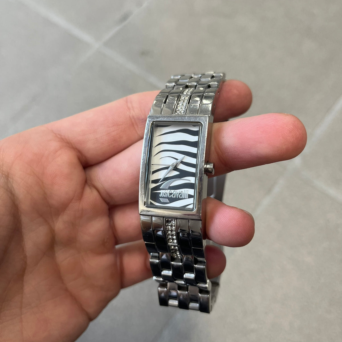 Just Cavalli Colas 2010’s Zebra Analog Watch is a stainless steel analog watch with a white and black zebra print dial and a silver Just Cavalli logo. The band matches the width of the case and has crystal details, and “Cavalli” is engraved on one side of the case.