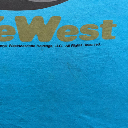 Kanye West 2012 Takashi Murakami 'Glow In The Dark Tour' Tee in light blue features the iconic bear with shutter glasses on the front. Below the graphic is yellow "kanYeWest" text and the 2007 Takashi Murakami/Kanye West licensing. Official merchandise from the 2012, this collectible tee includes the neck tag with Kanye logo and Mascotte Holdings licensing.