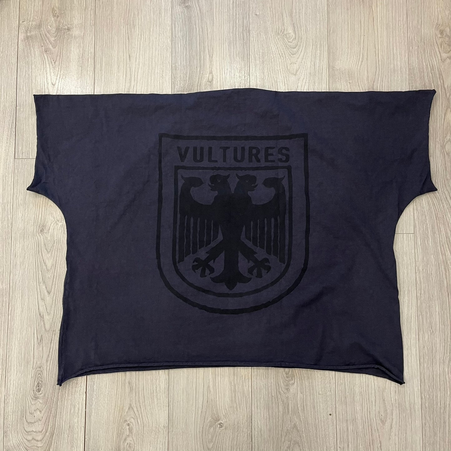 Kanye West Vultures Box Tee in navy features a large Vultures Eagles logo on the back and a smaller matching logo on the chest. Designed with an oversized, boxy silhouette, this T-shirt offers a relaxed fit. Made from high-quality, durable materials, it provides comfort for everyday wear while showcasing Yeezy’s distinctive style.