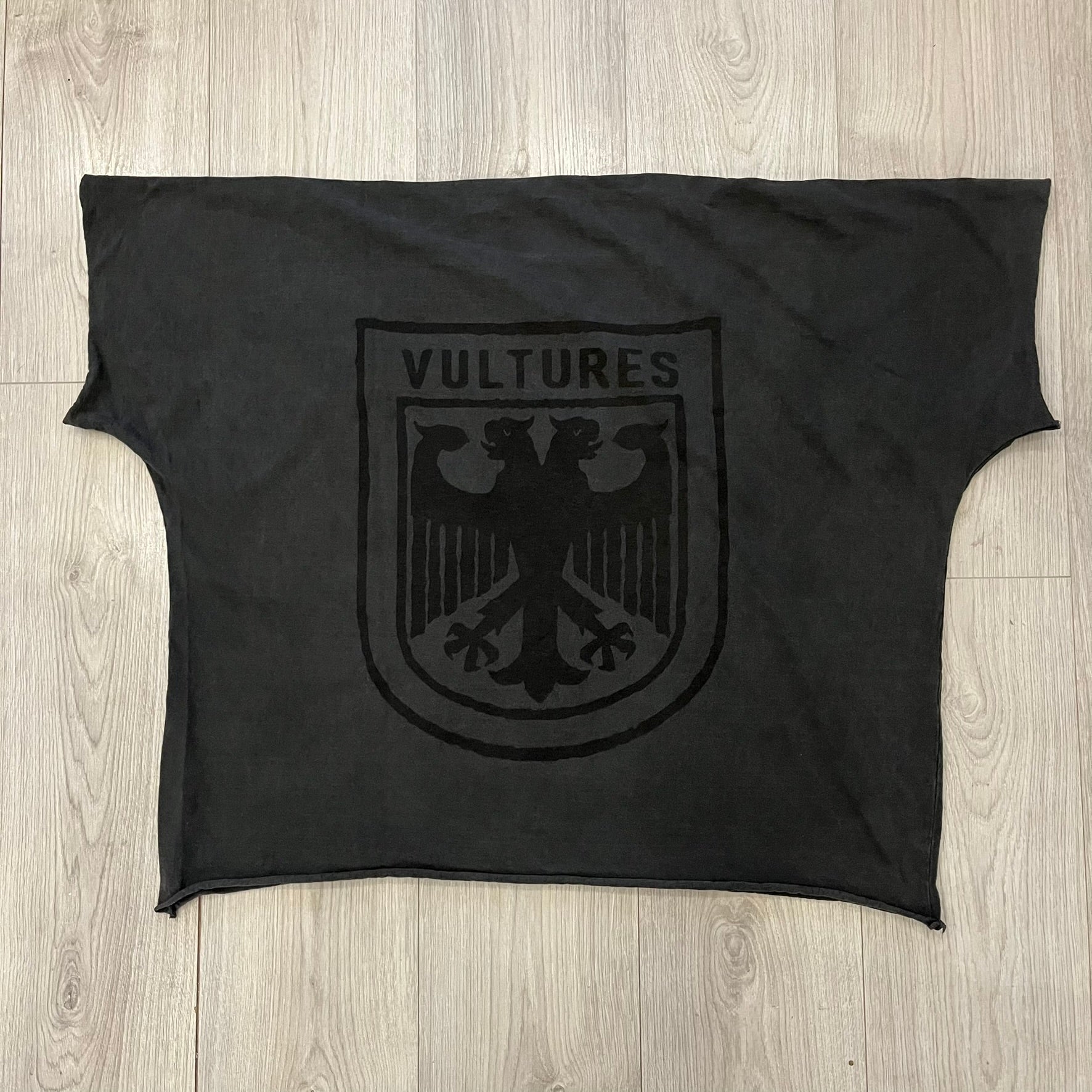 Kanye West Vultures Box Tee in washed black features a large Vultures Eagles logo on the back and a smaller matching logo on the chest. Designed with an oversized, boxy silhouette, this T-shirt offers a relaxed fit. Made from high-quality, durable materials, it provides comfort for everyday wear while showcasing Yeezy’s distinctive style.