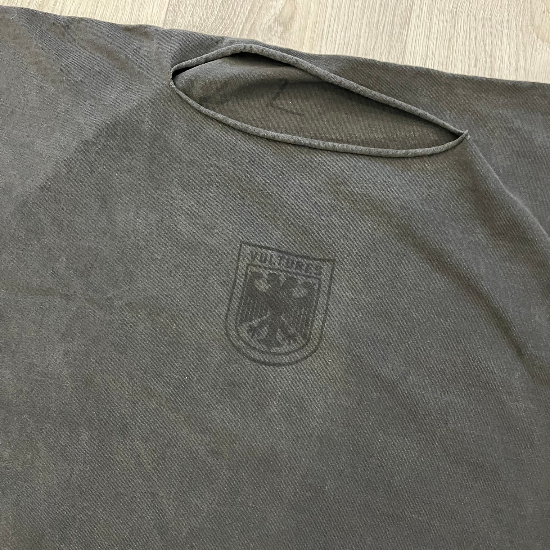 Kanye West Vultures Box Tee in washed black features a large Vultures Eagles logo on the back and a smaller matching logo on the chest. Designed with an oversized, boxy silhouette, this T-shirt offers a relaxed fit. Made from high-quality, durable materials, it provides comfort for everyday wear while showcasing Yeezy’s distinctive style.