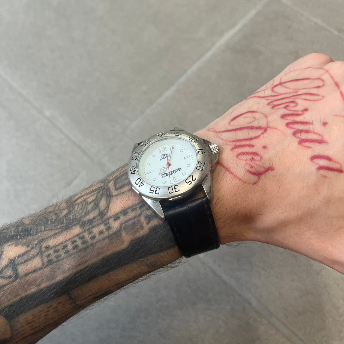 Kappa 2000's Quartz Analog Watch features black leather straps, a silver-tone case, and a white dial. The bezel is marked in five-minute increments from 5 to 55. The dial has a Kappa logo at the top and Kappa text below the center. The hour markers are represented by white dots and numerals. The watch has a stainless steel case back and is marked as a limited edition model.