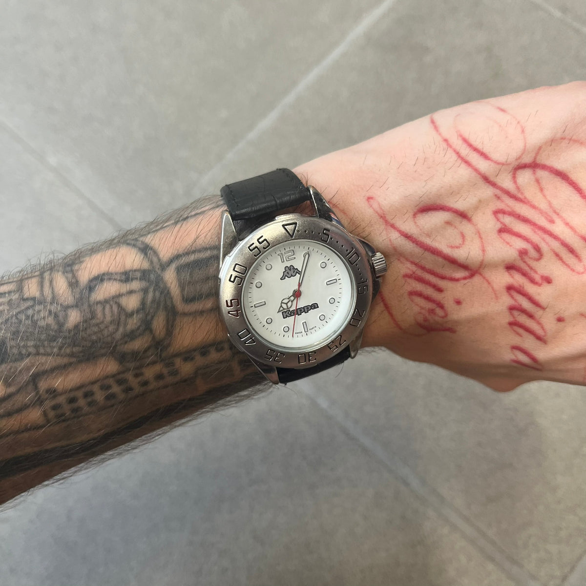 Kappa 2000's Quartz Analog Watch features black leather straps, a silver-tone case, and a white dial. The bezel is marked in five-minute increments from 5 to 55. The dial has a Kappa logo at the top and Kappa text below the center. The hour markers are represented by white dots and numerals. The watch has a stainless steel case back and is marked as a limited edition model.