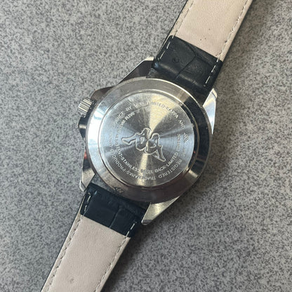 Kappa 2000's Quartz Analog Watch features black leather straps, a silver-tone case, and a white dial. The bezel is marked in five-minute increments from 5 to 55. The dial has a Kappa logo at the top and Kappa text below the center. The hour markers are represented by white dots and numerals. The watch has a stainless steel case back and is marked as a limited edition model.