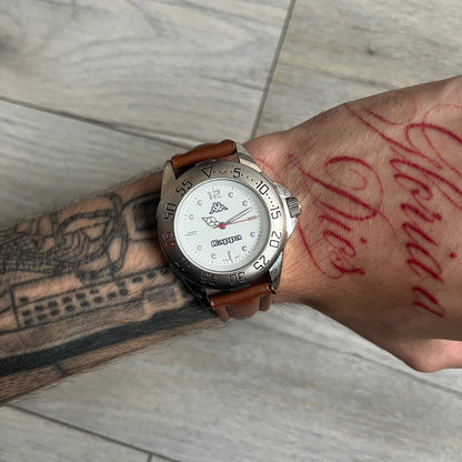 Kappa 2000s Quartz Analog Watch features brown leather straps, a silver-tone case, and a white dial. The bezel is marked in five-minute increments from 5 to 55. The dial has a Kappa logo at the top and Kappa text below the center. The hour markers are represented by white dots and numerals. The watch has a stainless steel case back and is marked as a limited edition model.